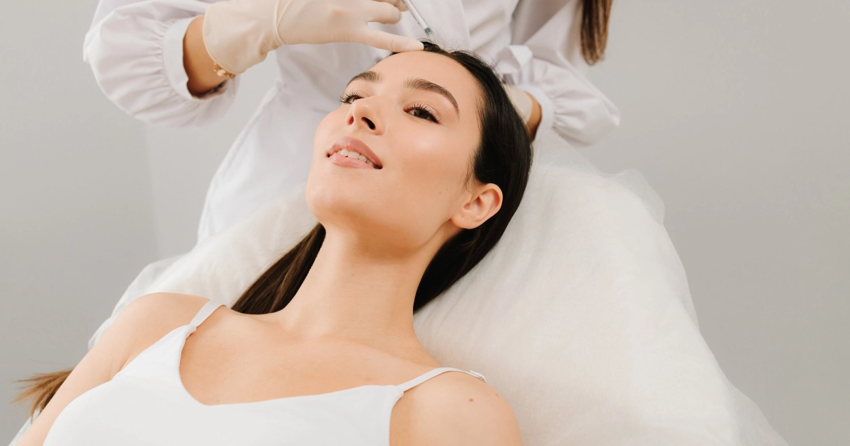 A woman lies comfortably on a treatment bed while a medical professional wearing gloves performs an injection on her forehead during Natural Growth Factor Injections in Horseshoe Bay, Texas.